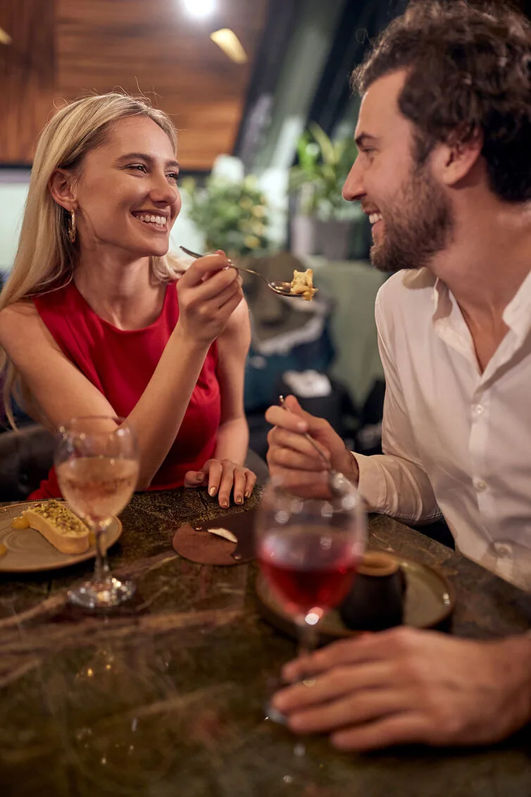 Two people laughing over dessert and wine at a restaurant table