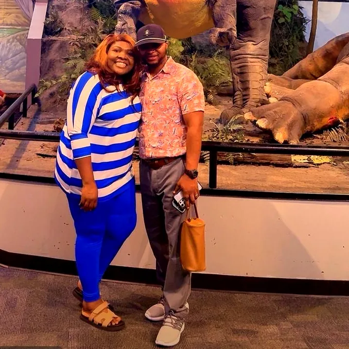 Samuel and his partner at a museum, under a dinosaur